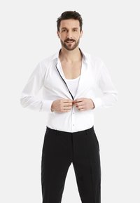 White dress shirt with black accents, slight sheen, and contrasting buttons. Worn partially open over a white undershirt and black trousers.