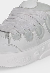 Close-up of a white sneaker with thick laces, mesh and leather panels, and embossed text "01 of 01" on the rubber sole.