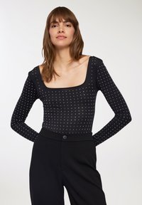 Body nero con maniche lunghe, scollatura quadrata e decorazioni in perline argentate disposte in un motivo a griglia. Design tessile aderente.