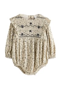 Romper beige à motif floral avec manches longues, épaules volantées et détail de corsage smocké mettant en valeur des accents noirs et des poignets élastiqués.