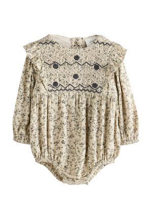 Beiger Jumpsuit mit Blumenmuster, langen Ärmeln, Rüschenschultern und gerafftem Oberteil, das schwarze Akzente und elastische Bündchen aufweist.