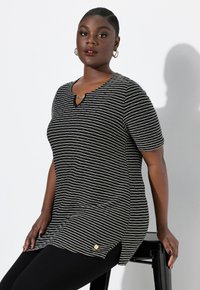 Top a rayas en blanco y negro con escote en forma de ojal, mangas cortas y aberturas laterales. Presenta un pequeño logo dorado en el dobladillo.