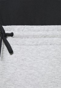 Pantalones deportivos grises con una cinturilla de algodón negra. Presenta un cordón con accesorios negros y una textura suave. Tejido gris claro con un patrón sutil.