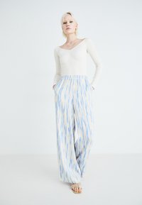White ribbed long-sleeve top paired with wide, patterned trousers in light blue and cream, featuring a loose fit and side pockets.