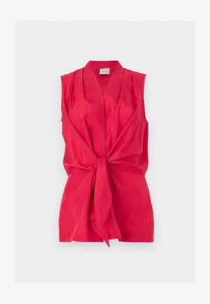 Blouse rouge vif sans manches avec un col en V profond et un détail de nouage sur le devant, présentée sur un fond plat et clair.