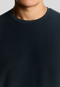 Donkerblauwe gestructureerde crewnecktrui met een fijn, geometrisch patroon en ribgebreide halslijn. Het materiaal lijkt zacht en lichtgewicht.