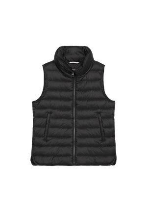Person trägt eine schwarze gesteppte ärmellose Weste über einem schwarzen Langarmshirt mit Händen in den Taschen, gezeigt vom Hals bis zu den Hüften vor einfarbigem Hintergrund.