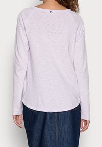 Ljuslila långärmad topp med en lätt böjd nederkant och en liten logodetalj på baksidan. Tillverkad av ett mjukt, texturerat tyg.