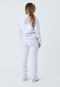 Grijze katoenen hoodie met een capuchon en bijpassende sweatpants. De outfit heeft elastische manchetten en een relaxed fit, gecombineerd met witte sportschoenen.
