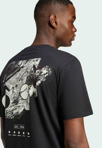 Svart bomull t-shirt med grafiska mönster på baksidan, inklusive cirkulära former och abstrakta mönster i vita och röda accenter.