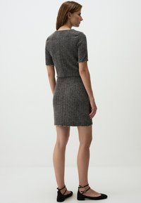 Robe en tweed gris à manches courtes, design ajusté, accents en perles le long de l'ourlet et silhouette droite. Assortie avec des chaussures plates noires.