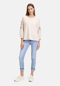 Sweatshirt beige clair avec des manches bouffantes et un imprimé graphique, associé à un jean skinny bleu clair et des baskets crème. Tenue décontractée simple.