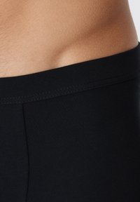 Ceinture élastique noire d'un boxer ajusté, présentant une texture lisse et légèrement brillante, avec des détails de couture subtils.
