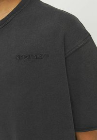 Svart bomullströja med rundad halsringning, kort ärm och broderad "ORIGINALS™" logotyp på framsidan i matchande tråd.