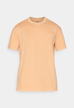 T-shirt de manga curta em algodão pêssego claro, com decote redondo e impressão discreta do logotipo no peito, apresentando uma textura suave e aveludada.