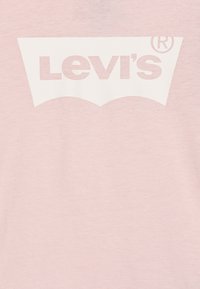Rožinė medvilninė marškinėlė su dideliu baltu Levi's® logotipu centre, virš teksto yra klasikinis įgaubtas dizainas.