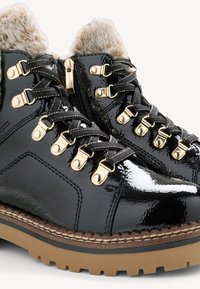 Fekete patentbőr bokacsizma arany kiegészítőkkel, fűzős záródással és műszőrme béléssel. Vastag, strukturált gumitalppal rendelkezik.