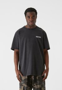 Sort oversized T-shirt med korte ærmer, slidte detaljer og broderet logo på venstre bryst. Kombineret med camo cargo bukser.