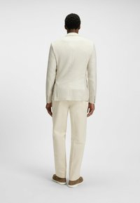 Hellbeige karierter Blazer, kombiniert mit passenden Hosen, im taillierten Schnitt und mit glatter Textur, ergänzt durch braune Schuhe.