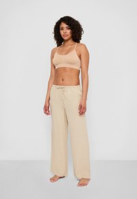 Beige crop top med tunna band som kombineras med ljusbeiga vida byxor med dragsko i midjan, tillverkade av ett mjukt material.