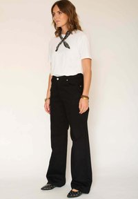 T-shirt blanc à manches courtes, pantalon noir taille haute et ballerines pointues noires avec accents argentés. Foulard noué autour du cou.