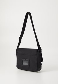 Borsa a tracolla nera con tracolla regolabile, tessuto testurizzato, pattina frontale e finestra ID trasparente. Presenta una forma rettangolare elegante.