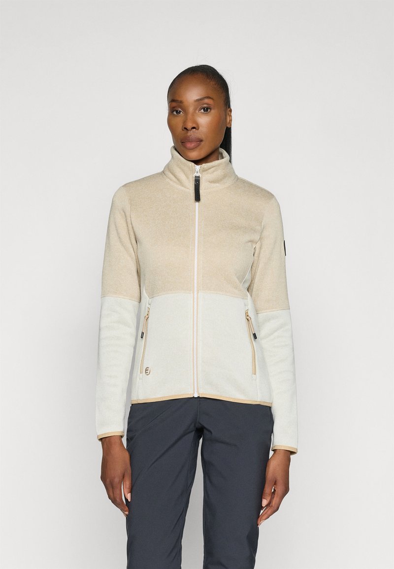 Chaqueta de forro polar ligera en beige y crema, con un alto cuello, dos bolsillos con cremallera y ribete contrastante a lo largo de las costuras.