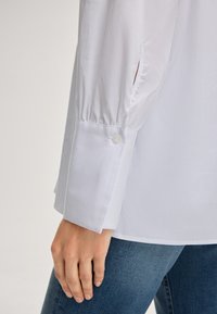 Witte button-up shirt met lange mouwen, voorzien van gathered cuffs; gladde textuur; gecombineerd met donkere denim.