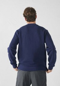 Sudadera azul marino con mangas largas, escote redondo y puños de canalé. Fabricada con material suave y de textura lisa. Sin marcas visibles.