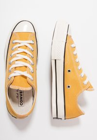 Gula kanvas sneakers med vita snören, gummitåhättor och svart kantning. Har runda öljett-hål och texturerade sulor för bra grepp.