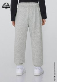 Szare spodnie dresowe z elastycznym pasem i mankietami, o miękkiej fakturze. W połączeniu z białymi trampkami, widok z tyłu.