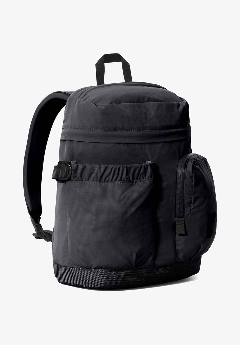 Sac à dos noir de forme arrondie, en tissu, avec des bretelles ajustables, une poche latérale en mesh, une poignée supérieure et un fond texturé.