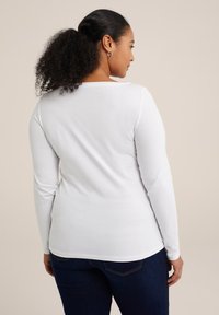 Weißes Langarmshirt mit Rundhalsausschnitt, taillierter Passform, weichem Material und glattem Stoff, kombiniert mit dunkelblauen Jeans.