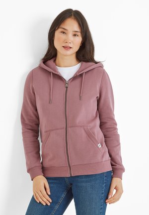 Pink hooded sweatshirt with a zipper, front pockets, and ribbed cuffs and hem. Worn over a white shirt, featuring a small logo tag on the side.