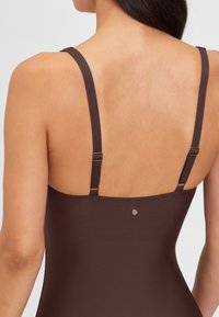Brauner Einteiler Badeanzug mit dünnen verstellbaren Trägern, der eine glatte Textur und ein kleines Logodetail auf dem Rücken aufweist.