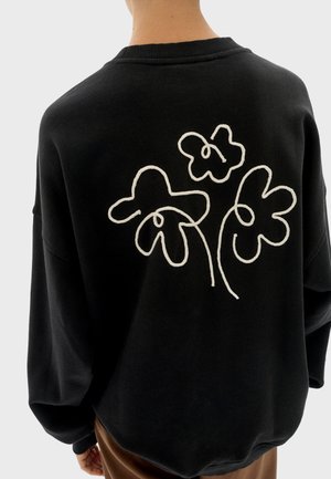 Felpa nera dal taglio oversize, con ricamo floreale bianco sulla schiena. Collo e polsini a costine. Tessuto morbido e strutturato.