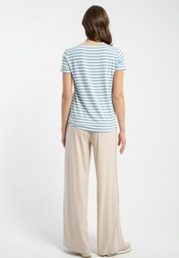 Pasiasta, jasnoniebieska i biała koszulka z krótkim rękawem w parze z beżowymi spodniami typu wide-leg, prezentująca luźny krój i miękką fakturę materiału.