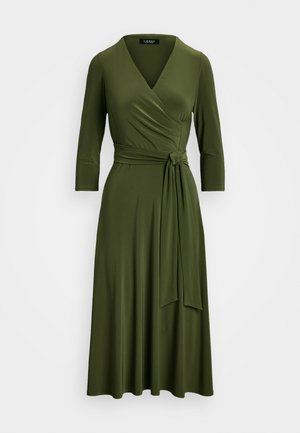 Oliwkowa sukienka kopertowa uszyta z miękkiego materiału, z rękawami o długości trzech ćwierć, detalem w postaci przewiązki w talii oraz rozkloszowanym dolnym brzegiem.