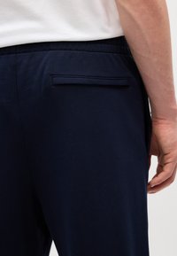 Pantalones de chándal azul marino con un detalle de bolsillo trasero. Fabricados con una tela suave y con una cinturilla elástica, diseñados para la comodidad y la facilidad de movimiento.