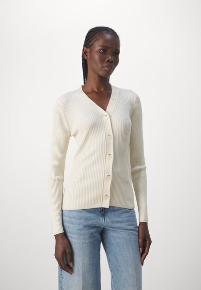 Kremfarget ribbestrikket cardigan med V-hals, med knappdetaljer foran og lange ermer, sammen med lyseblå jeans.