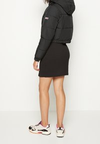 Sort cropped puffer-jakke med hætte, elastiske manchetter, båret over en tætsiddende sort kjole, parret med cremede og pink sneakers.