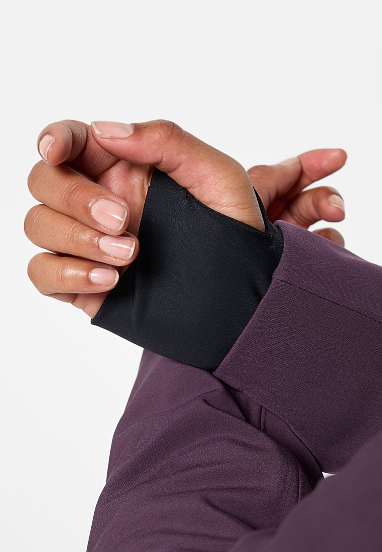 Primo piano di due mani con unghie naturali, una delle quali tira un polsino con foro per il pollice nero su un indumento a maniche lunghe viola, coprendo il polso.