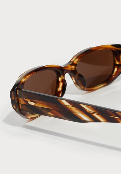 Lunettes de soleil écaille de tortue marron avec des verres ronds, dotées de branches à motifs et de subtils accents en or.