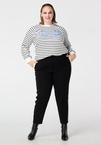 Gestreepte sweatshirt in wit, zwart en blauw; gecombineerd met zwarte broek met crèmekleurige zijstrepen; glanzende stof; enkellaarsjes.