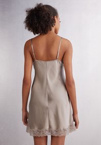 Satin-nattlinne i dämpad taupe med delikat spetsdetalj i fållen; har justerbara spagettiband och en mjuk, slät textur.