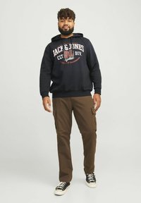 Black hoodie with a front print, paired with brown cargo pants featuring side pockets and black sneakers with white soles.