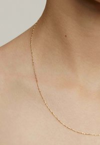 Collar de cadena de oro con un diseño alargado y enlazado reposando sobre la piel, con una textura suave y un brillo sutil.