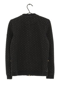 Černá prošívaná bunda s malými zlatými švy, dlouhými rukávy, žebrovan ými manžetami a spodním lemem, zavěšená na černém kovovém ramínku.