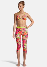 Le haut de bikini présente un motif floral rose avec des bretelles fines ; les leggings sont multicolores avec des motifs floraux assortis et une taille néon verte.