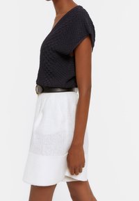 Marineblauw gebreid top met een brede halslijn, gecombineerd met een witte geweven rok met een subtiele horizontale patroon en een zwarte riem.